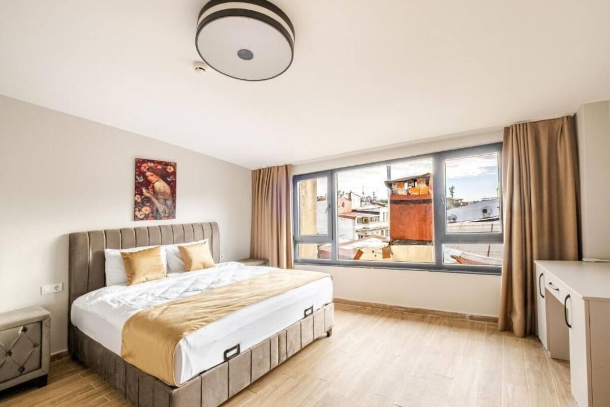 Habitación de hotel con cama, ventana con vistas, lámpara en el techo y un cuadro en la pared.
