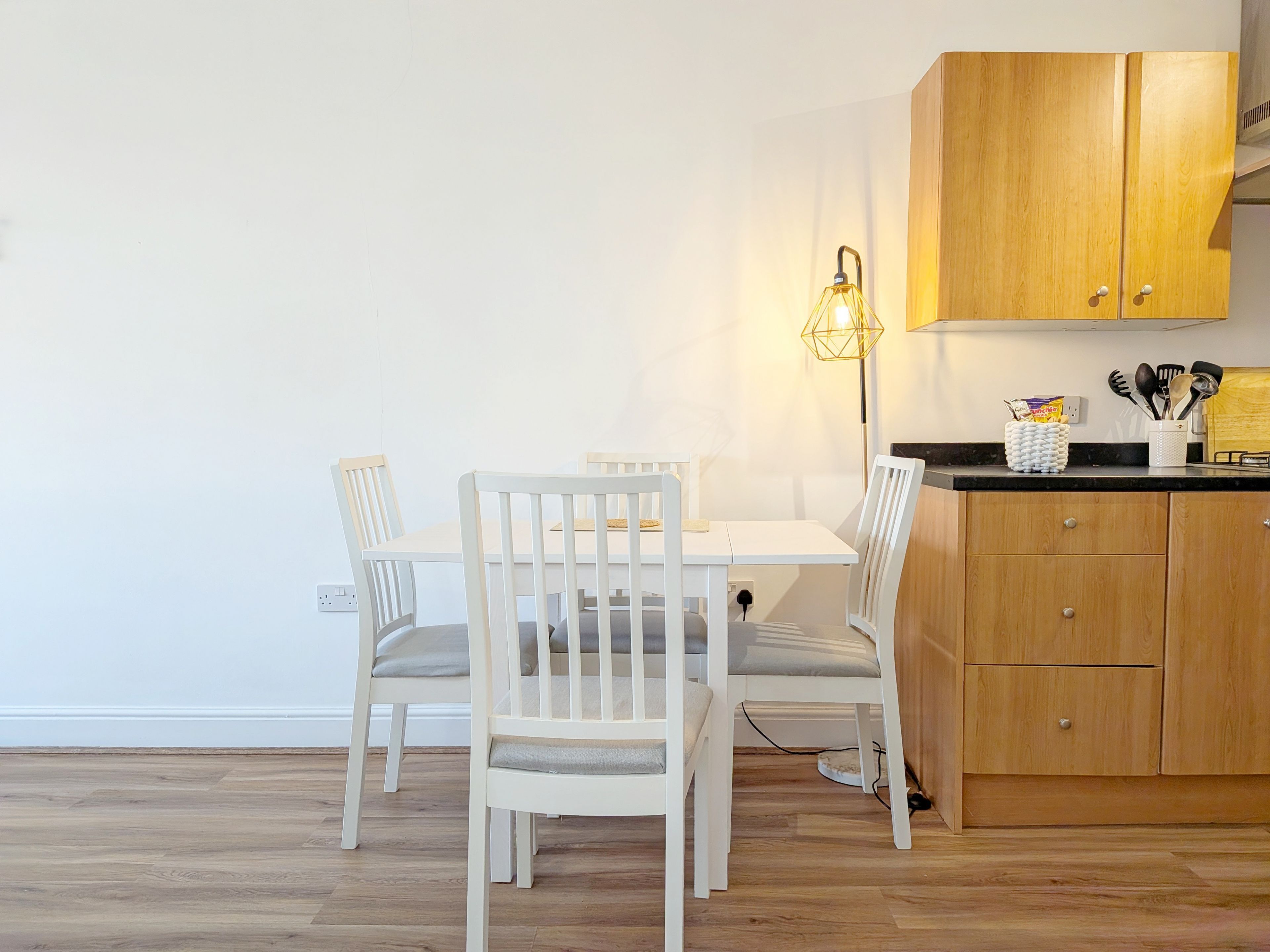 Un coin repas avec une table et des chaises blanches, un meuble en bois et un lampadaire.