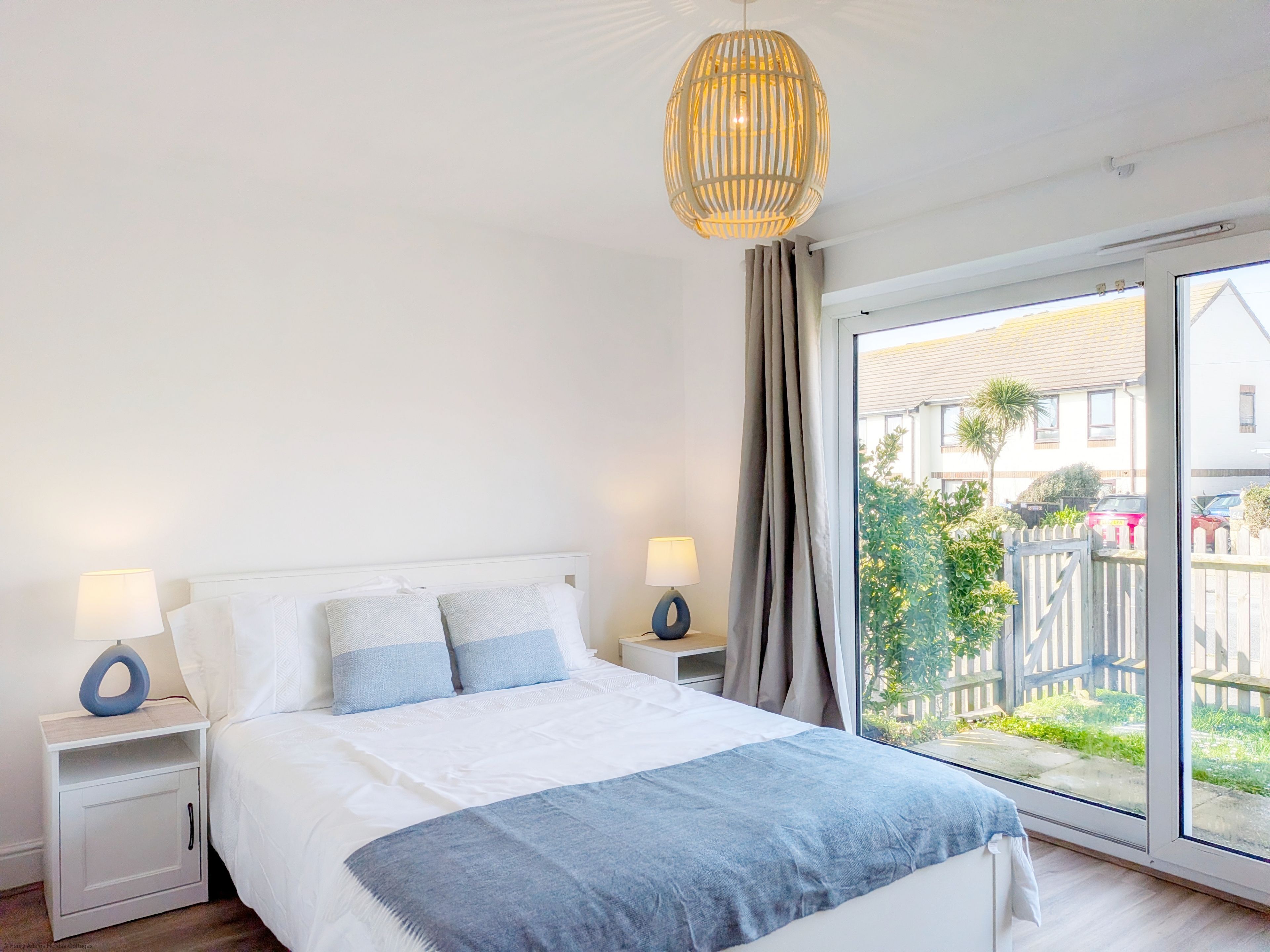 Un dormitorio con cama, mesitas de noche, lámpara colgante, ventana con cortinas y vistas al exterior.