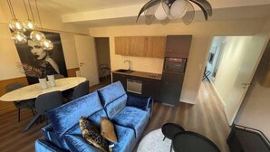 A modern living room with a blue sofa, a dining table, and a kitchen area.