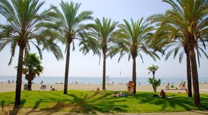 A beach with palm trees, people sunbathing, and the ocean in the background. - Malaga Refino Apartment With Rooftop Pool (Málaga)