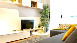 A modern living room with a flat-screen TV, a grey sofa with yellow cushions, a white coffee table, and a potted plant. - Malaga Refino Apartment With Rooftop Pool (Málaga)