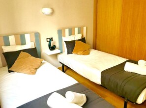 Zwei Einzelbetten mit gestreifter Kopfteil, ein Nachttisch mit Lampe und ein Holzschrank.