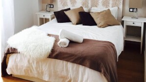 A neatly made bed with a white and brown blanket, two bedside lamps, and a headboard with a leaf pattern. - Malaga Refino Apartment With Rooftop Pool (Málaga)