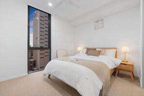 A bedroom with a large bed, two bedside lamps, a view of a building through a window, and a small picture on the wall. - Massive Stadium View | 2BR | Free Parking|CBD (Kangaroo Point)