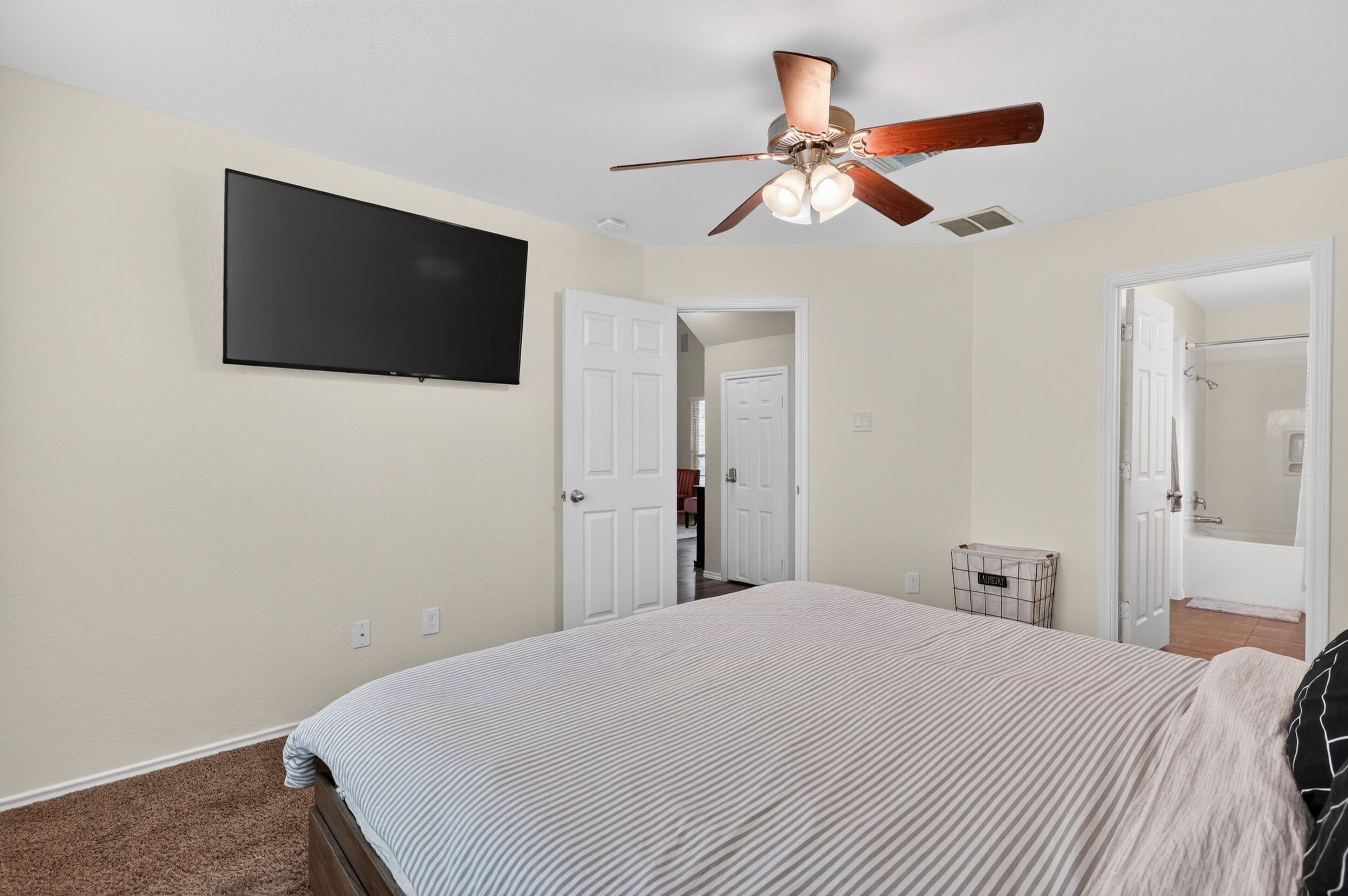 A bedroom with a bed, a ceiling fan, a TV, and two doors leading to other rooms.