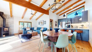 A modern living room with a fireplace, a dining area with a wooden table and chairs, and a kitchen with dark cabinets and stainless steel appliances. - Chateau Sans Nom #35 4 Bedroom Condo (Mammoth Lakes)