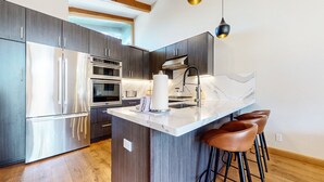 A modern kitchen with stainless steel appliances, a marble countertop, and wooden bar stools. - Chateau Sans Nom #35 4 Bedroom Condo (Mammoth Lakes)