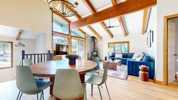 A spacious room with a large wooden dining table, chairs, a blue sofa, and a stone fireplace. - Chateau Sans Nom #35 4 Bedroom Condo (Mammoth Lakes)
