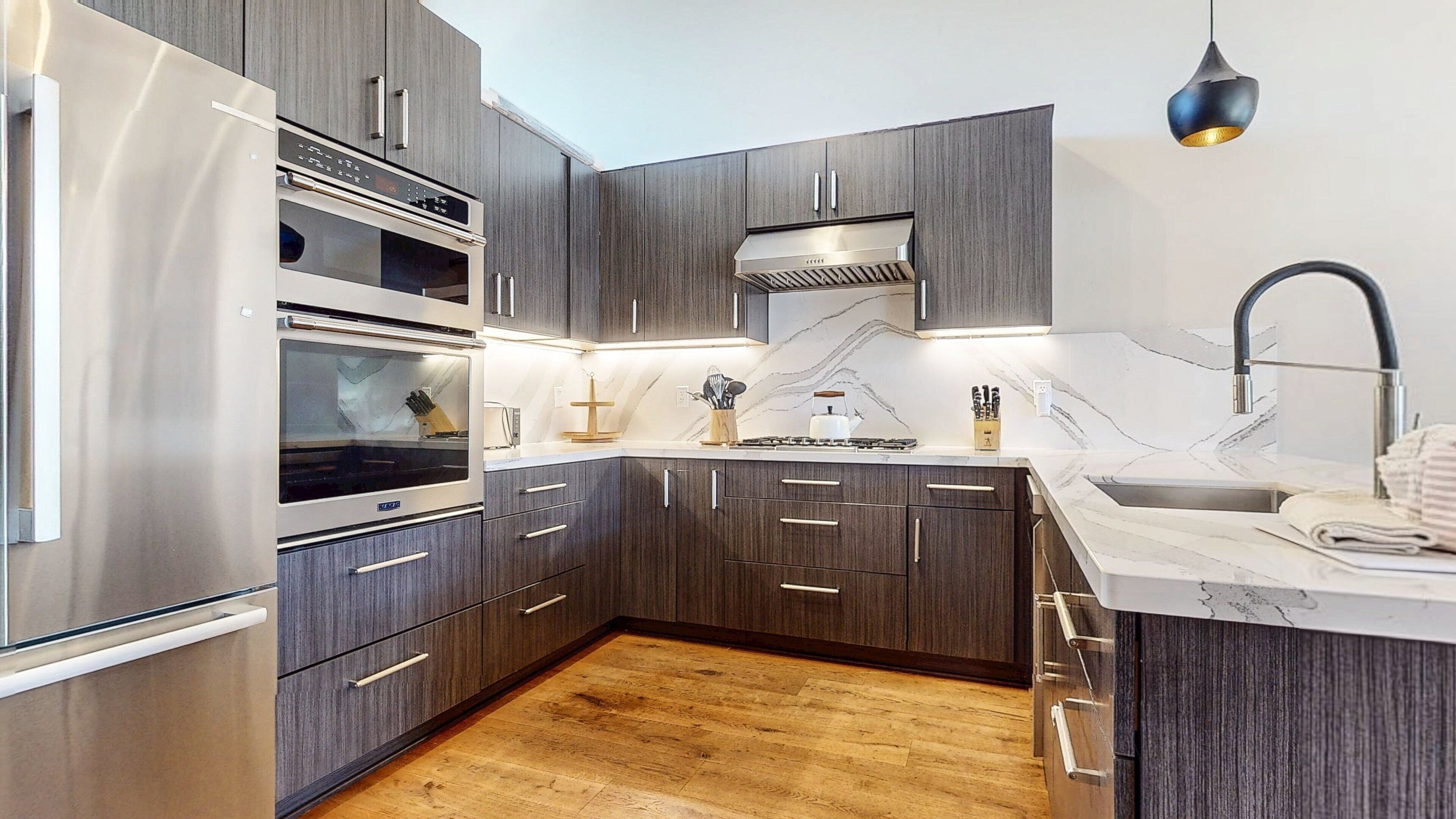 Una cocina moderna con armarios de madera oscura, electrodomésticos de acero inoxidable y una salpicadera de mármol.