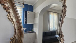 Ein Zimmer mit einem großen, verzierten Spiegel, einer Küchenzeile mit blauer Wand und einem dunkelgrauen Sofa.