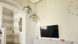 Ein modernes Wohnzimmer mit Flachbildfernseher, weißem Lowboard, Holzböden und einem Spiegel.