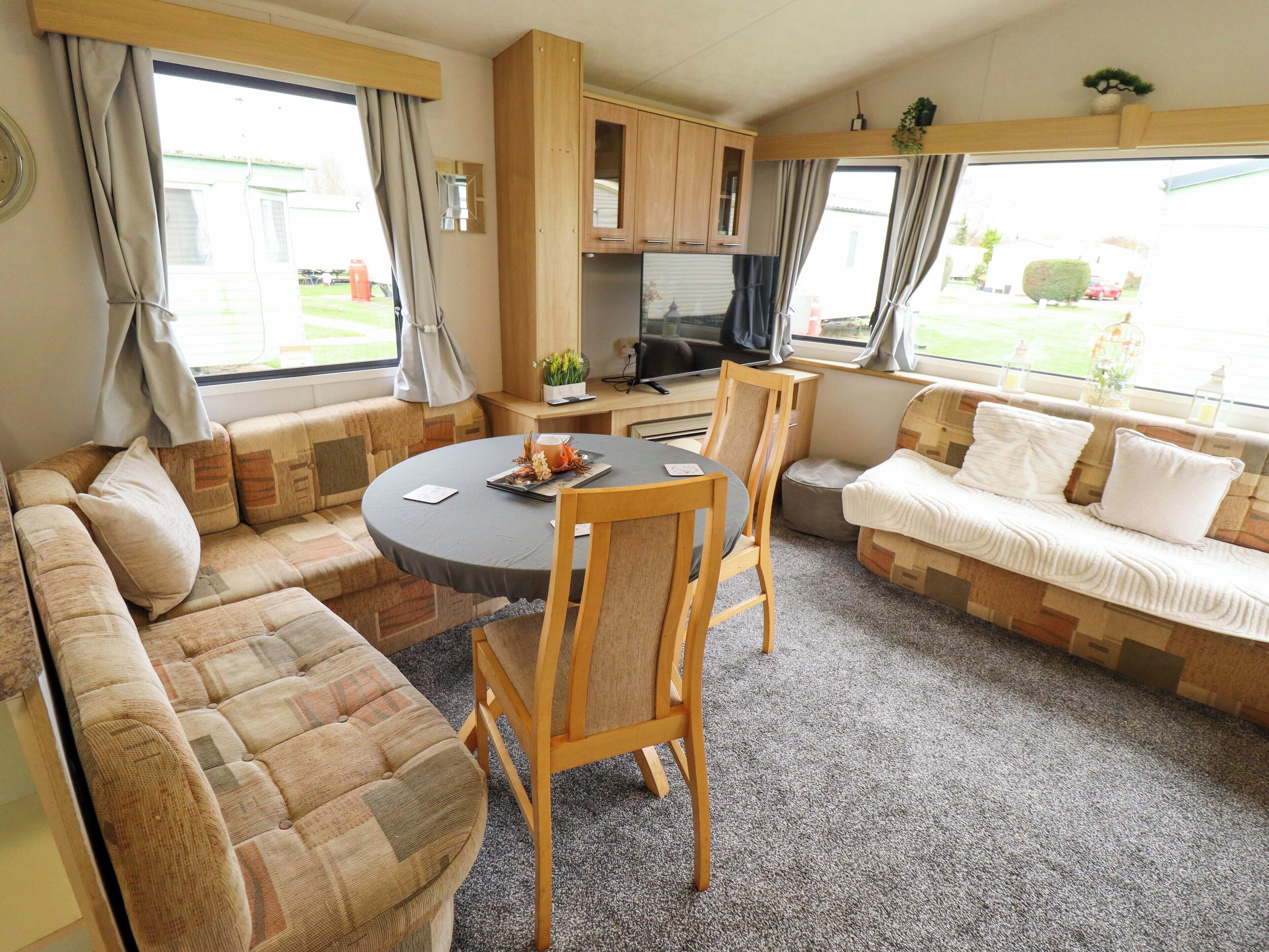 Een compact interieur van een camper, met een bank, eettafel, stoelen, een televisie en een kitchenette.