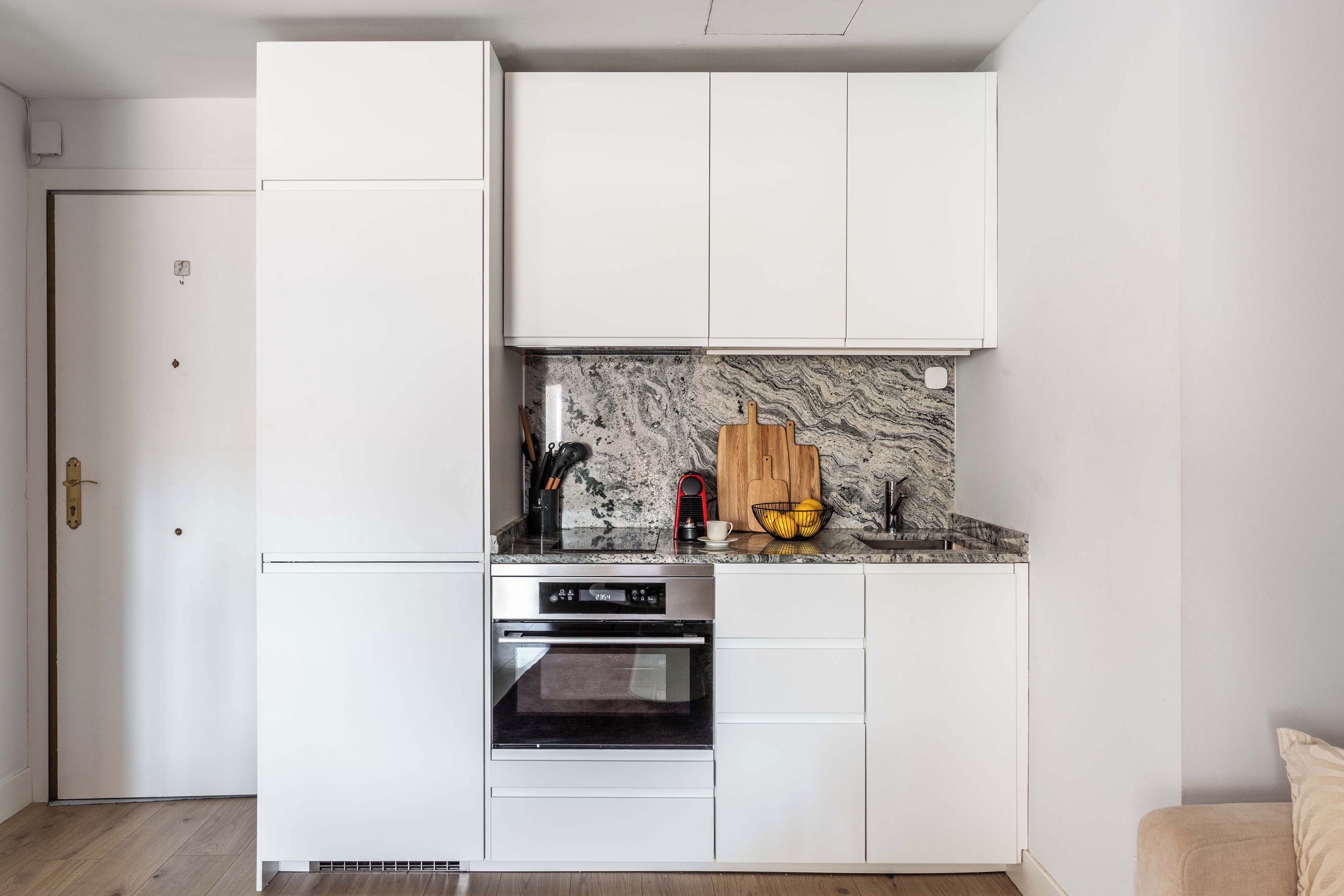 A compact kitchen with white cabinetry, a built-in oven, and a marble backsplash.