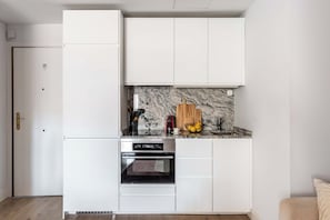 A compact kitchen with white cabinetry, a built-in oven, and a marble backsplash. - This elegant one-bedroom apartment in the heart of Justicia—one of Madrid’s most vibrant and exclusive neighborhoods—combines contemporary design, comfort, and a sophisticated atmosphere ideal for extended stays (MADRID)