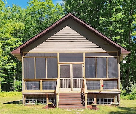A wooden cabin with a pitched roof, large windows, and a front porch.. Perfect 2-bedroom house in Evart for a secluded relaxing getaway!