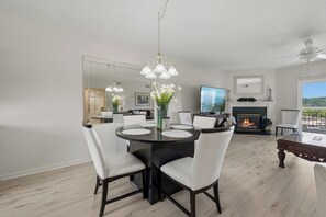 A dining area with a round table, white chairs, and a chandelier. There is a fireplace with a TV in the background. - Three Bedroom Two Bathroom Condo in Pigeon Forge| Near Dollywood| Sleeps 8 (Pigeon Forge)
