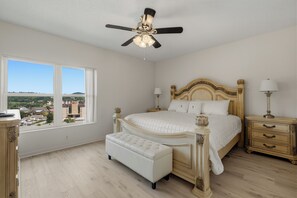 Un dormitorio con una cama grande, un banco, una mesita de noche y un ventilador de techo.