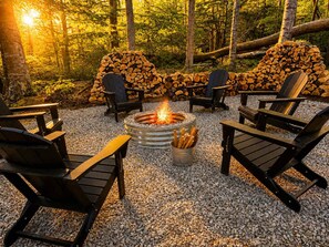Un área de estar al aire libre con una chimenea rodeada de sillas y una pila de leña.