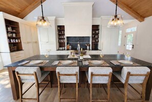 A large kitchen island with a marble countertop, wooden chairs, and pendant lighting.