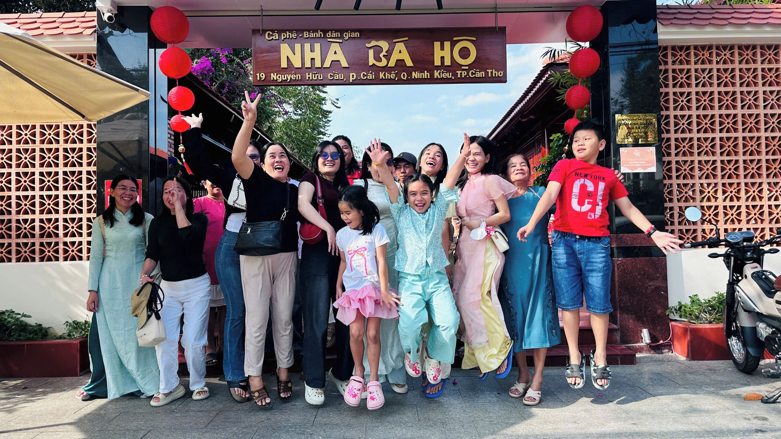 A group of people posing in front of a building with a sign that reads 'NHA BA HO'.