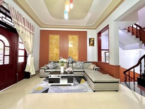 A modern living room with a sectional sofa, a coffee table, and a staircase. - Mekong INN (Can Tho)