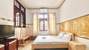A hotel room with a bed, a TV, a wooden nightstand, and a window with curtains. - Mekong INN (Can Tho)