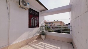A balcony with a potted plant, a window with a red frame, and an air conditioning unit mounted on the wall. - Mekong INN (Can Tho)
