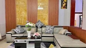 A modern living room with a sectional sofa, a glass coffee table, and a patterned rug. - Mekong INN (Can Tho)