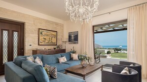 A living room with a blue sofa, a wooden coffee table, a chandelier, and a view of the sea. - Stunning Mediterranean Villa for 6 (Kissamos)