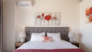 A neatly made bed with a red throw blanket, two bedside lamps, a grey upholstered headboard, and a wall-mounted air conditioner. - Stunning Mediterranean Villa for 6 (Kissamos)
