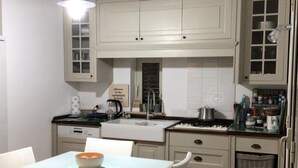Una cocina con armarios blancos, una mesa de comedor con sillas, una lámpara colgante y suelo de ladrillo.
