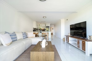 Una sala de estar moderna con un sofá blanco, una mesa de centro de madera y un televisor sobre un mueble blanco.
