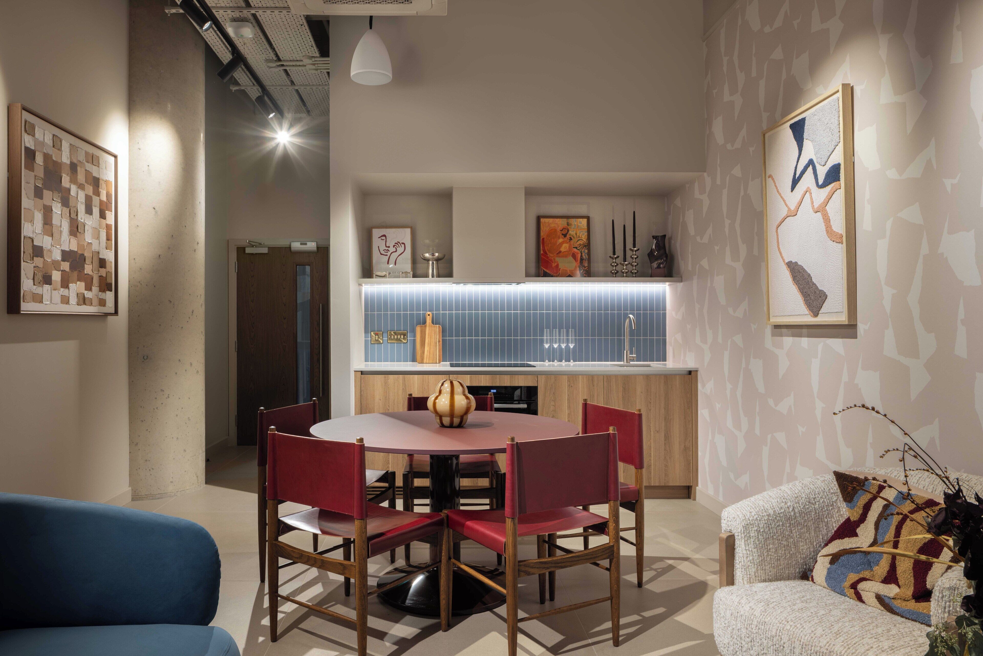 A modern interior with a round dining table, red chairs, a blue sofa, and a patterned wall.