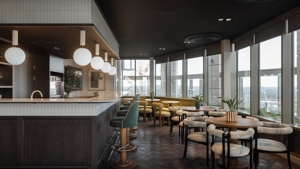 A modern bar area with a bar counter, seating, and large windows offering a city view. - StayCozy Studio Apartments in Acton (London)