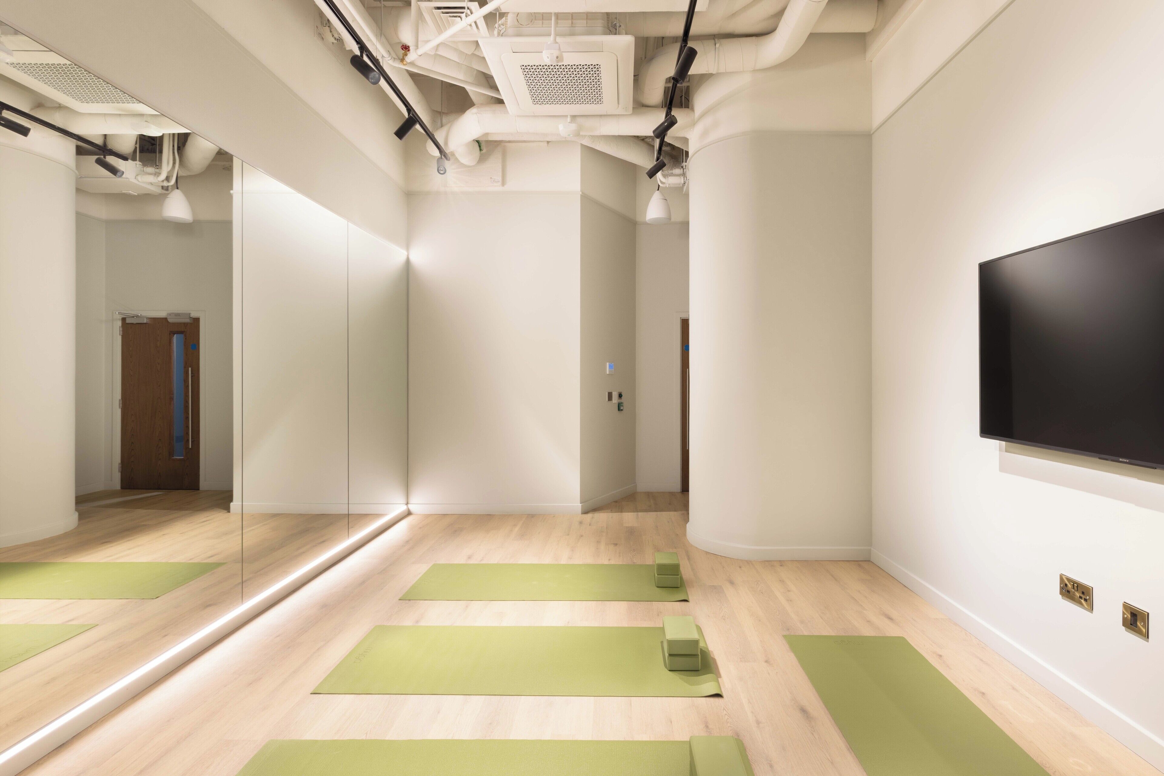 A room with a large mirror, green yoga mats, a flat-screen TV, and a wooden floor.