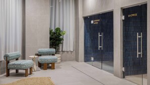A modern bathroom with two blue shower doors, a large potted plant, and two upholstered chairs. - StayCozy Studio Apartments in Acton (London)