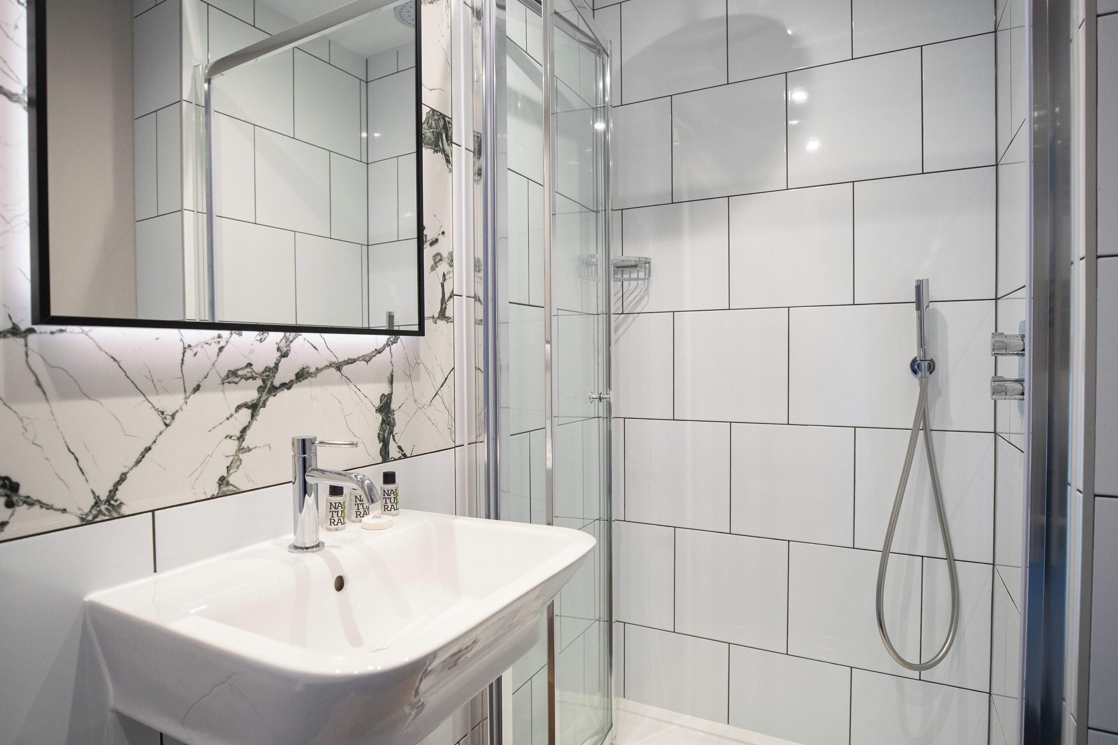 A modern bathroom with a white sink, a glass shower enclosure, and a marble-tiled wall.