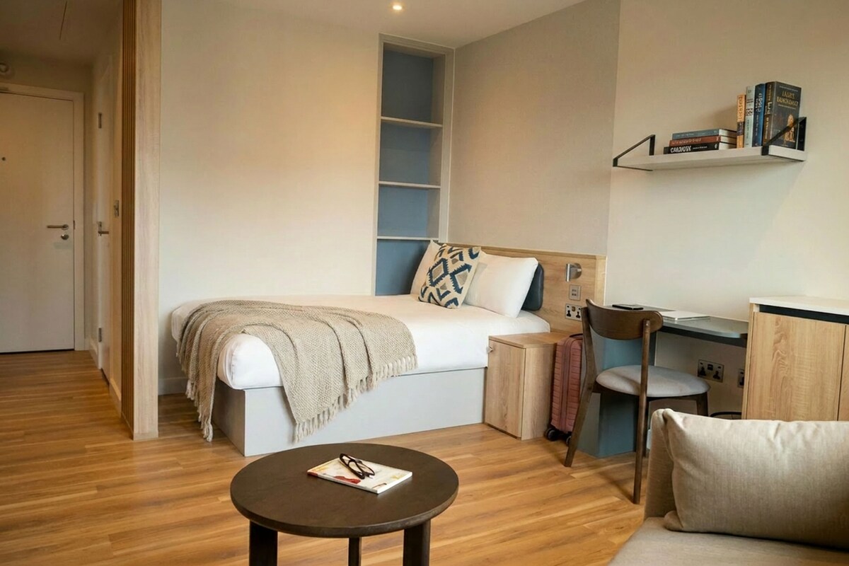 A bedroom with a bed, bedside table, chair, and a small desk with a chair.