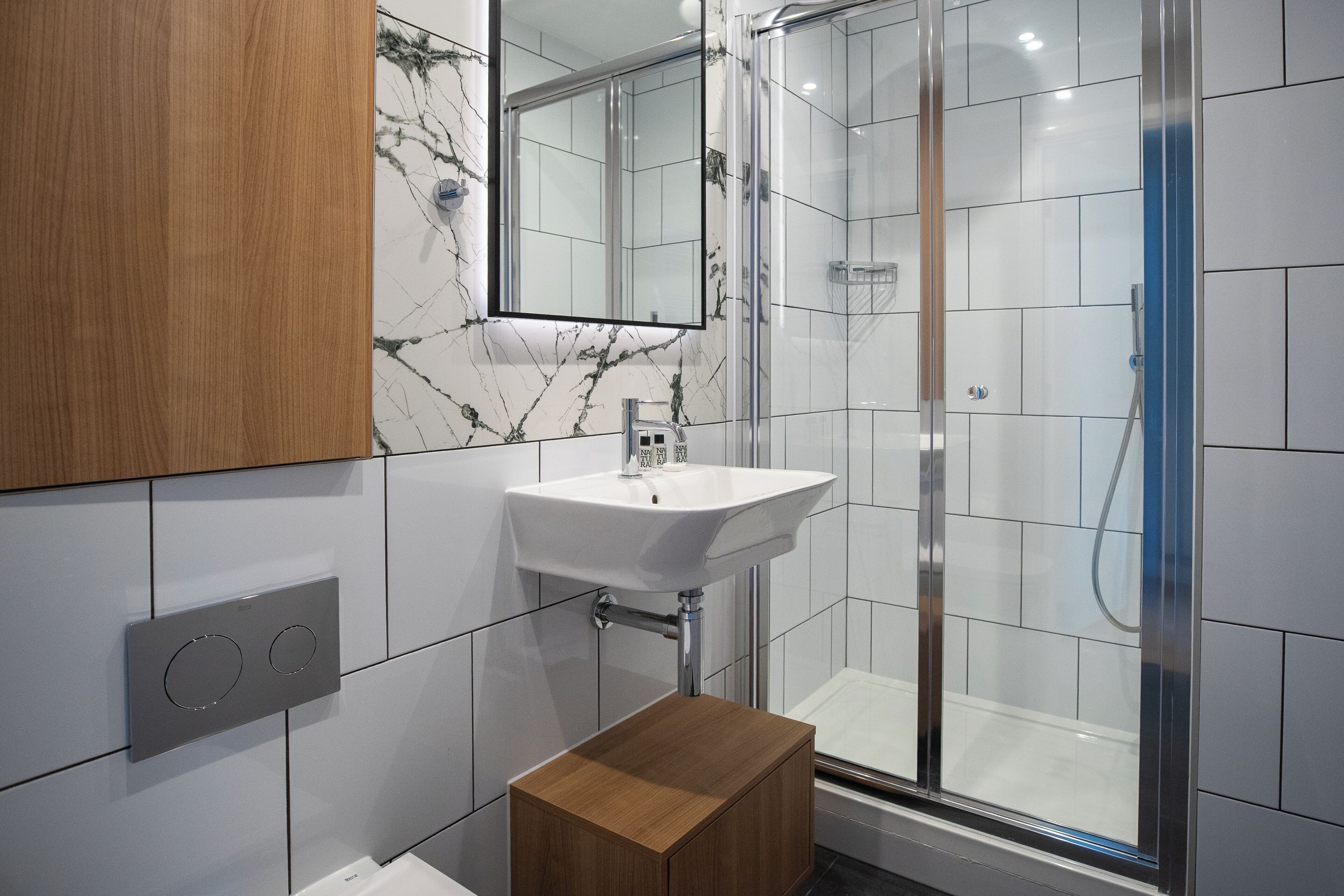 Un baño moderno con un lavamanos blanco, un espejo, cabina de ducha y un mueble de madera.