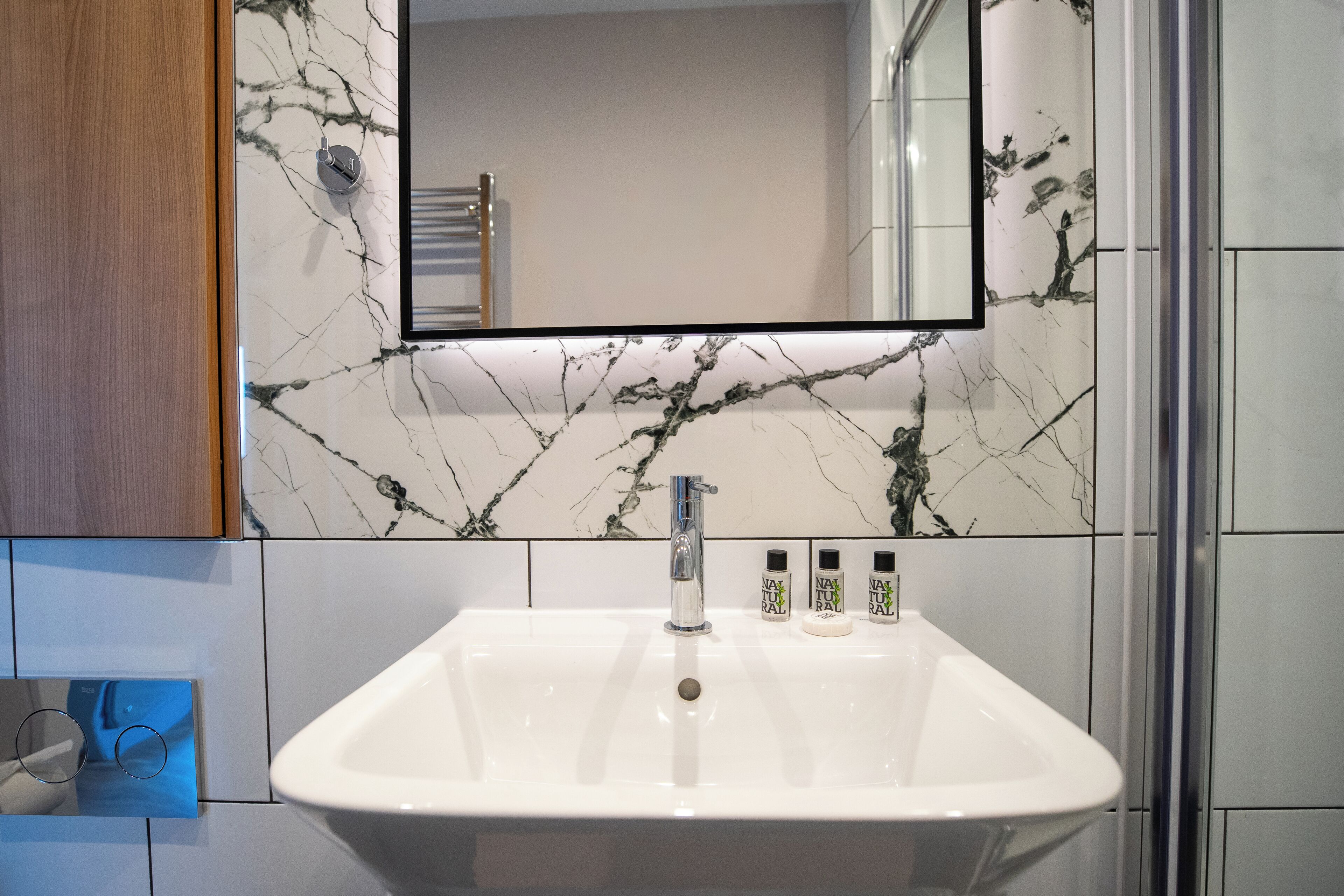 Un baño con lavamanos blanco, un espejo y paredes con diseño de mármol.