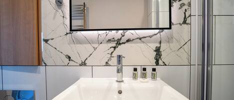 Un baño con lavamanos blanco, un espejo y paredes con diseño de mármol.