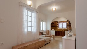 A spacious living room with a wooden bench, a sofa, and a kitchen area in the background. - Naousa Central House, Paros (Paros)