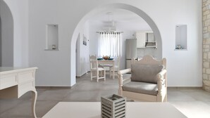 A minimalist living room with a white desk, a cushioned armchair, and a dining area with a table and chairs. - Happy  2-Bedroom sea view House, pool/jacuzzi! (Livadia)