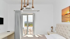 Quarto com cama, televisão, escrivaninha e vista para o exterior.