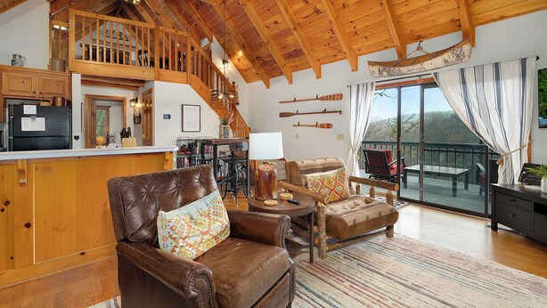 Ein geräumiger Wohnbereich mit hoher Decke, Holzbalken, einer Küche und einem Balkon mit Blick.