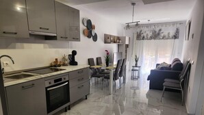 Een moderne keuken met een inbouwoven, een eethoek met een glazen tafel en stoelen, en een zithoek met een bank en een televisie.