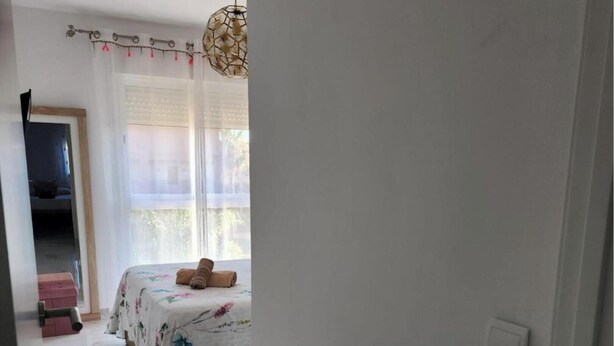 Een slaapkamer met een bed, een hanglamp en een raam met gordijnen.