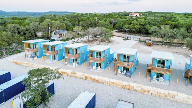 A row of blue cabins with balconies, surrounded by trees and a gravel path. - Hill Country Views | Canyon Lake Retreat (Canyon Lake)
