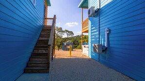 A narrow pathway between two blue buildings with a wooden staircase leading to a balcony. - Hill Country Views | Canyon Lake Retreat (Canyon Lake)